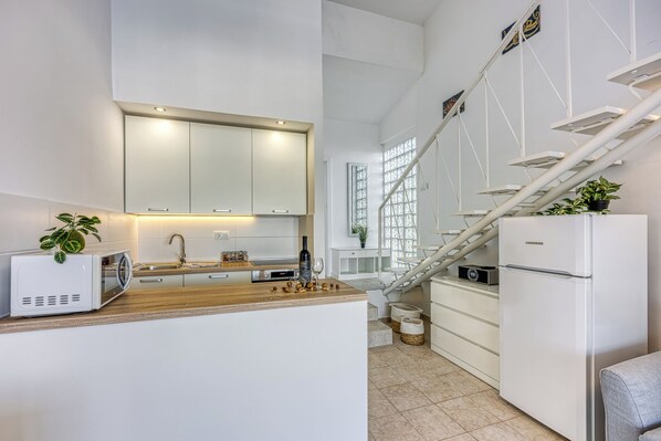 A modern kitchen with white cabinets, a microwave, a sink, and a refrigerator.