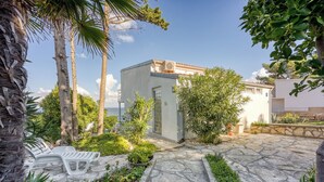 Un sendero de piedra que lleva a un edificio blanco con tejado de azulejos, rodeado de vegetación y palmeras.
