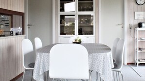 Un coin repas avec une table ronde, des chaises blanches, une suspension et une horloge au mur.