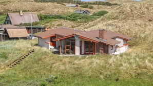 Une maison avec un toit rouge, de grandes fenêtres et un escalier menant à l’entrée.