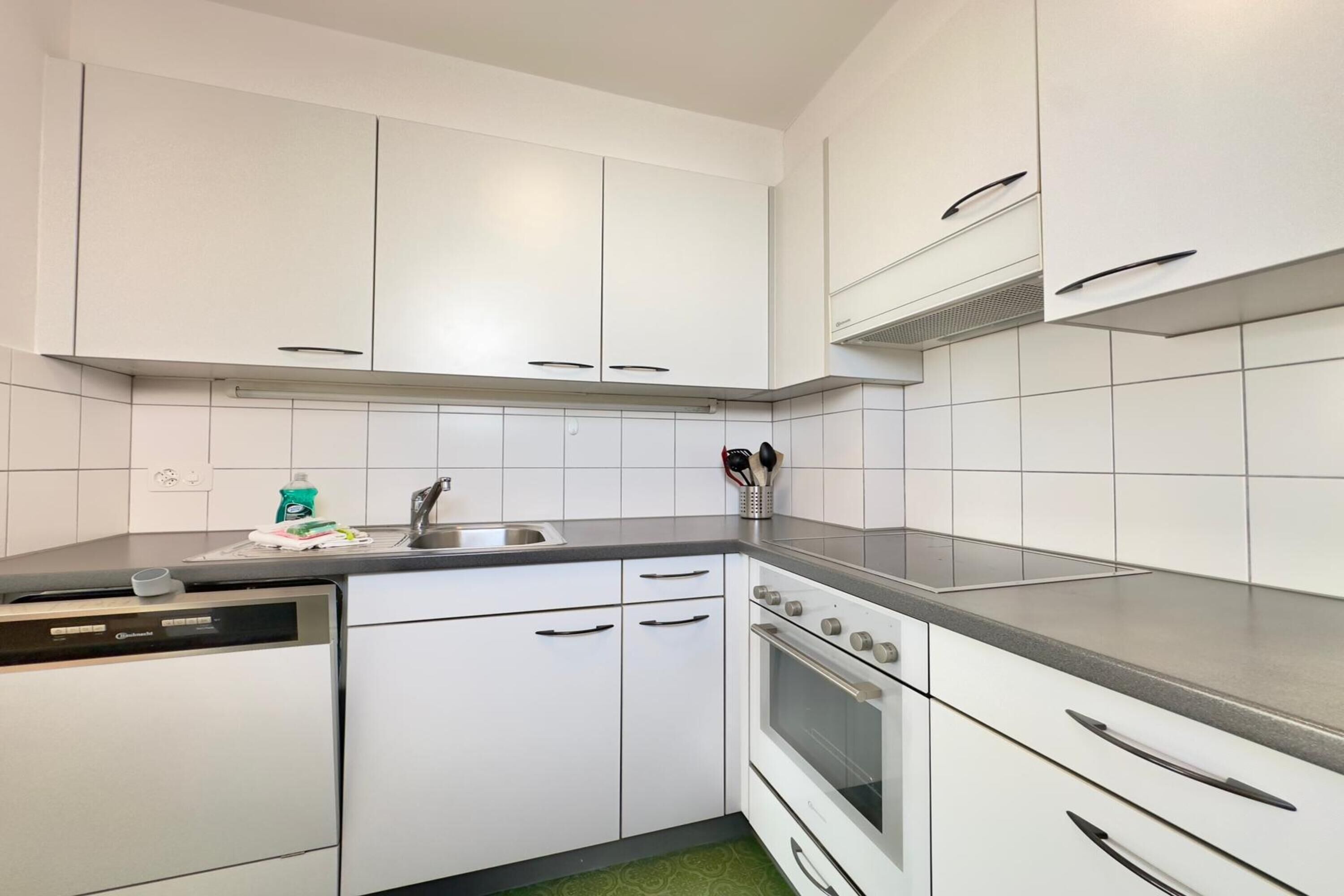 Una cocina compacta con armarios blancos, horno empotrado y lavavajillas.