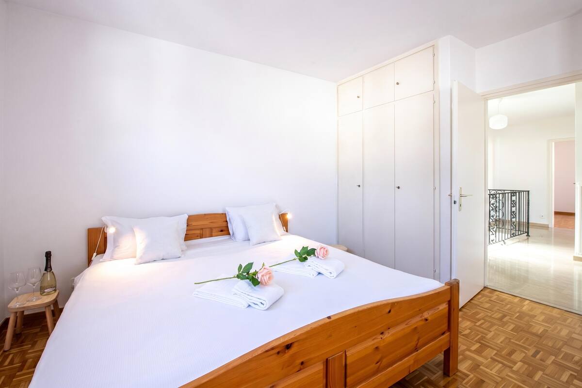 Una cama bien hecha con sábanas blancas, un cabecero de madera y una mesita de noche con una botella y vasos.