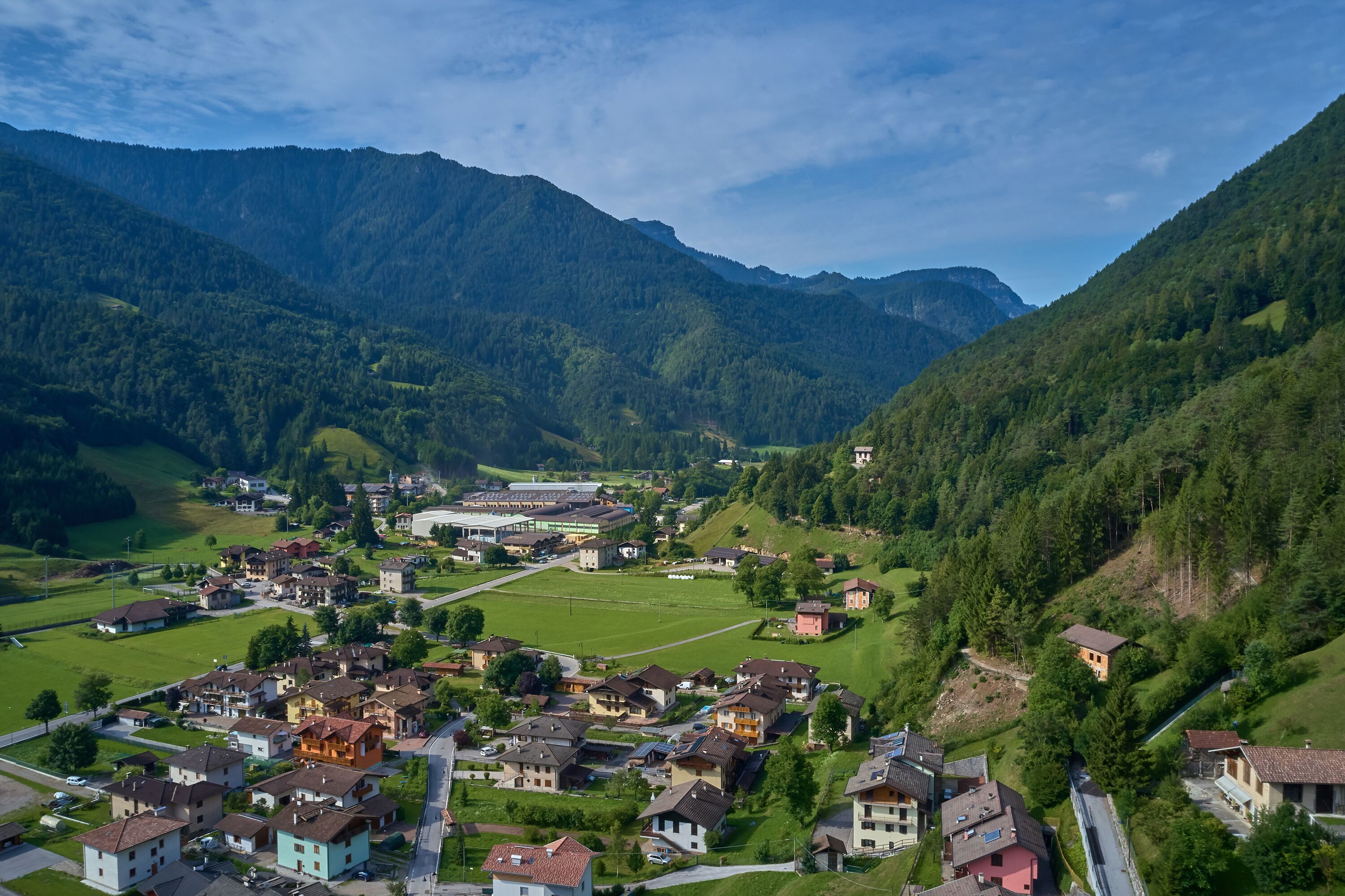 A mountainous village with residential buildings, a sports field, and a small church.