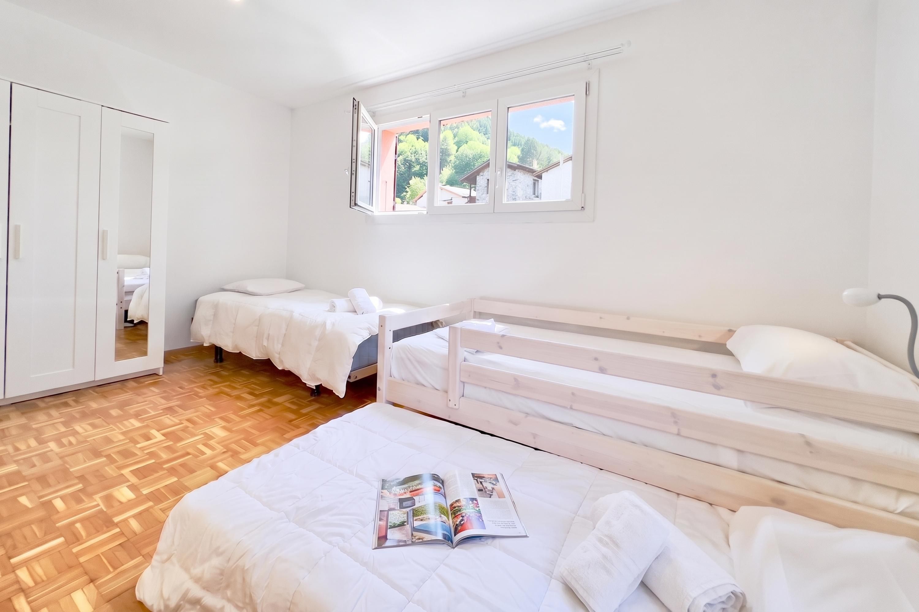 Une chambre avec deux lits, une armoire et une fenêtre donnant sur un espace verdoyant.