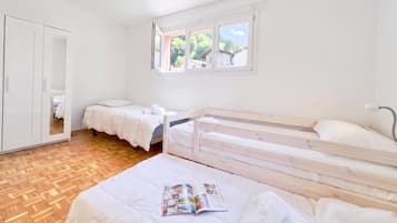 Une chambre avec deux lits, une armoire et une fenêtre donnant sur un espace verdoyant.