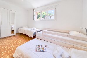 A bedroom with two beds, a wardrobe, and a window with a view of greenery.