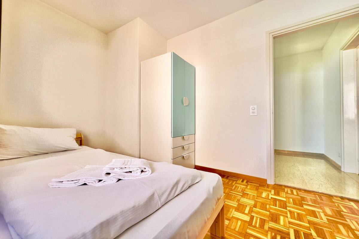 Una habitación de hotel con una cama, piso de madera, un armario y una puerta que da a otra habitación.