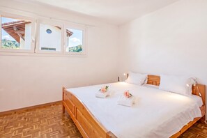 A single-bed room with a wooden headboard, white bedding, and a view of a mountainous landscape through a window. - Casa Carolina (Losone)