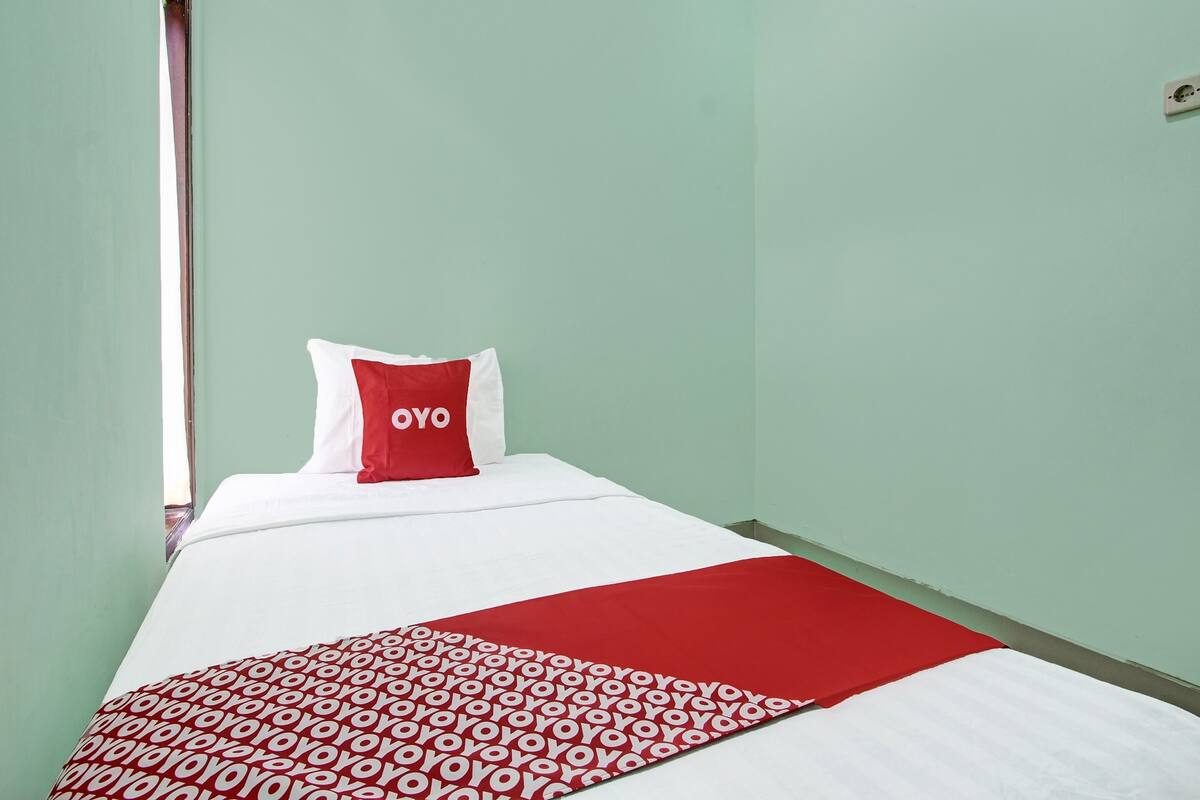 Ein Einzelbett mit einer weiß-rot gemusterten Tagesdecke, einem roten Kopfkissen mit dem Aufdruck "YOYO" und einer roten Decke.