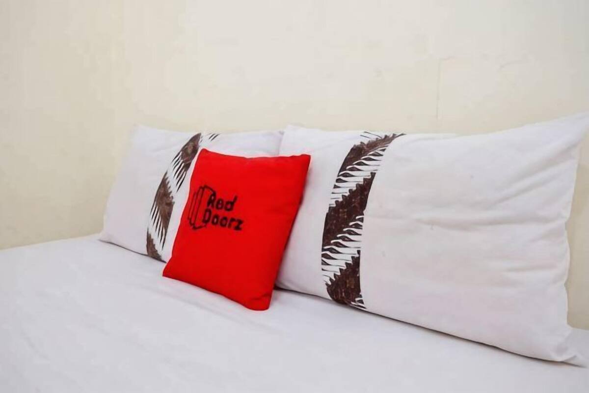 Ein Bett mit weißer Bettwäsche und einem roten Kopfkissen mit Text.