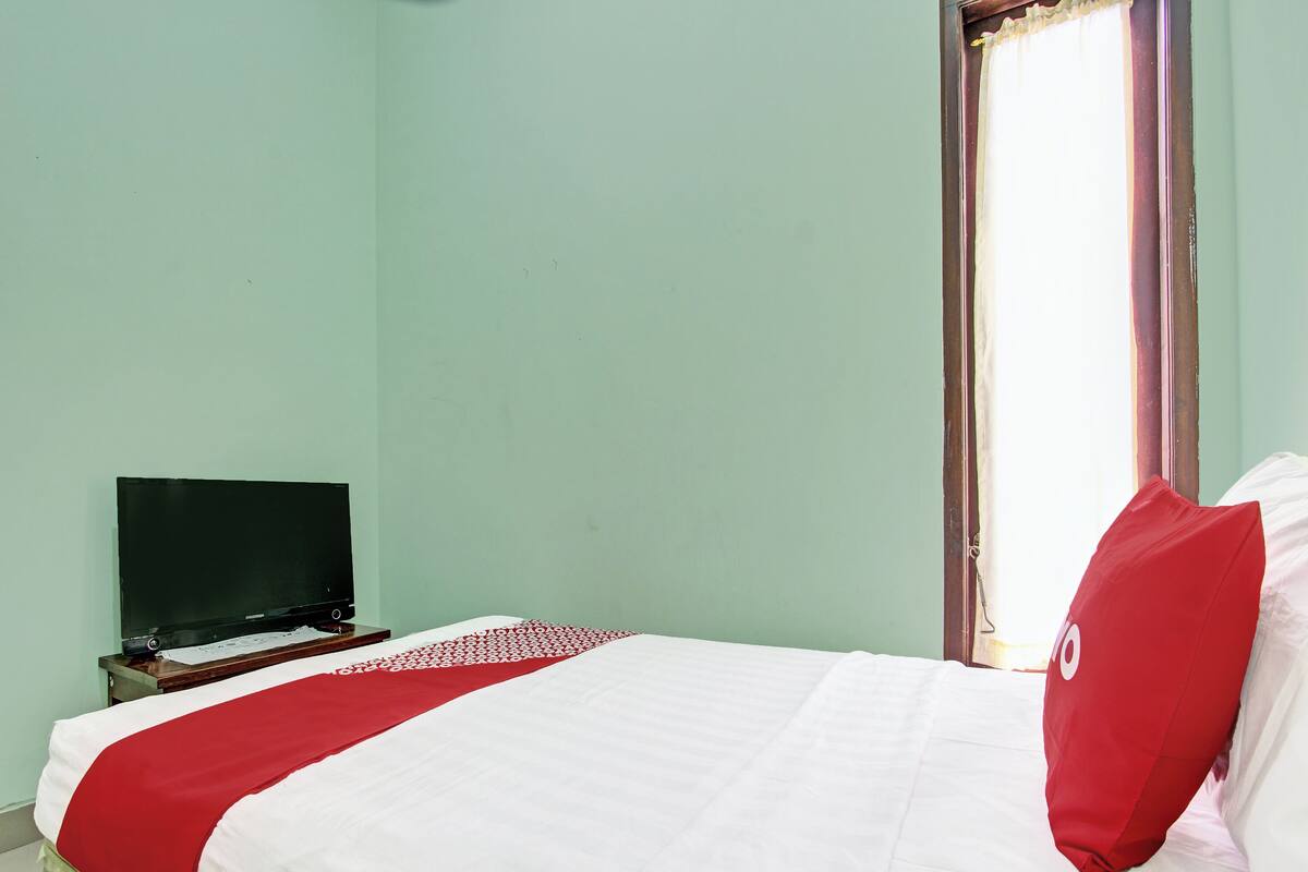 Ein Zimmer mit einem Bett, einem Fernseher auf einem Schrank und einem Vorhangfenster.