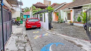 A narrow street with a red car parked on the side, a gated entrance, and buildings with traditional architecture. - Hotel O Gita Graha Guest House Syariah (Yogyakarta)