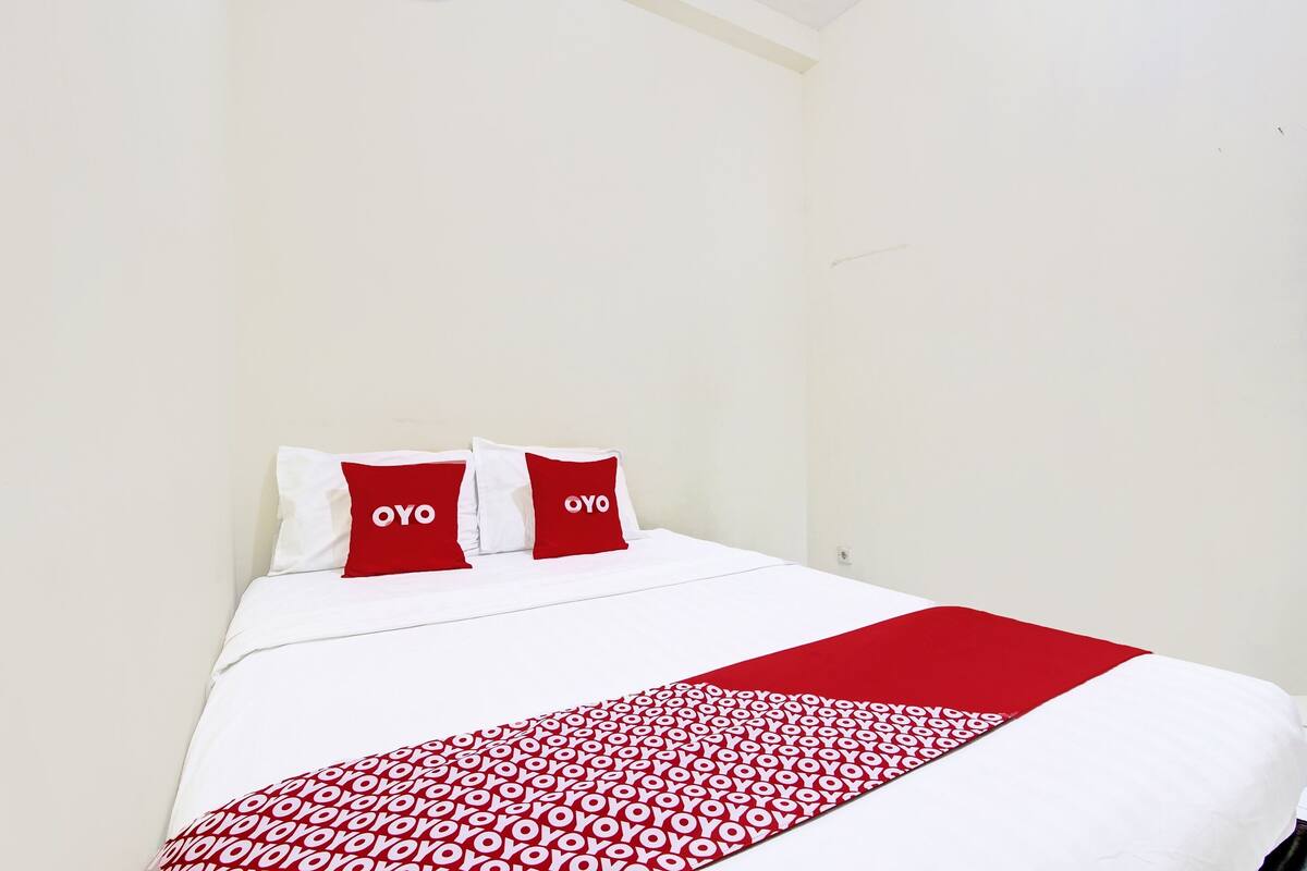 Ein Hotelzimmer mit Bett, weißen Wänden und roten Kissen mit dem Schriftzug "OYO".