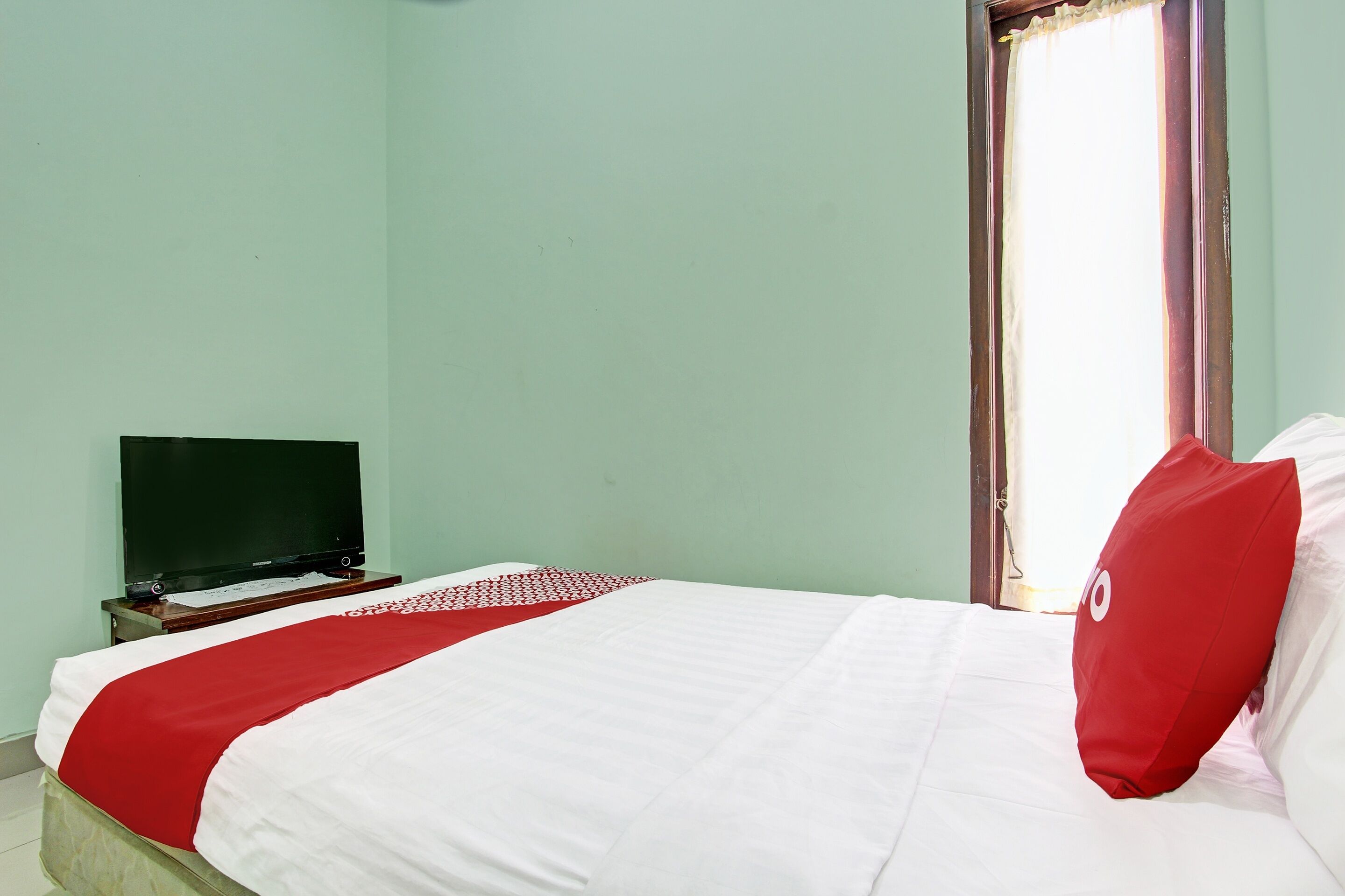 A neatly made bed with a white and red bedspread, a red pillow, and a television on a small table beside the bed.