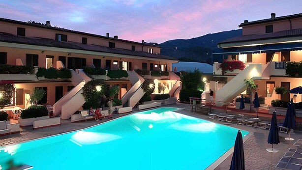 Piscina con edificios adyacentes, una escalera y mobiliario exterior.