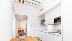 A modern kitchen with white cabinetry, a wooden dining table, and a built-in oven. - Candelaria10 - Apartamento Noble, a peaceful retreat within the heart of Cádiz (Cádiz)