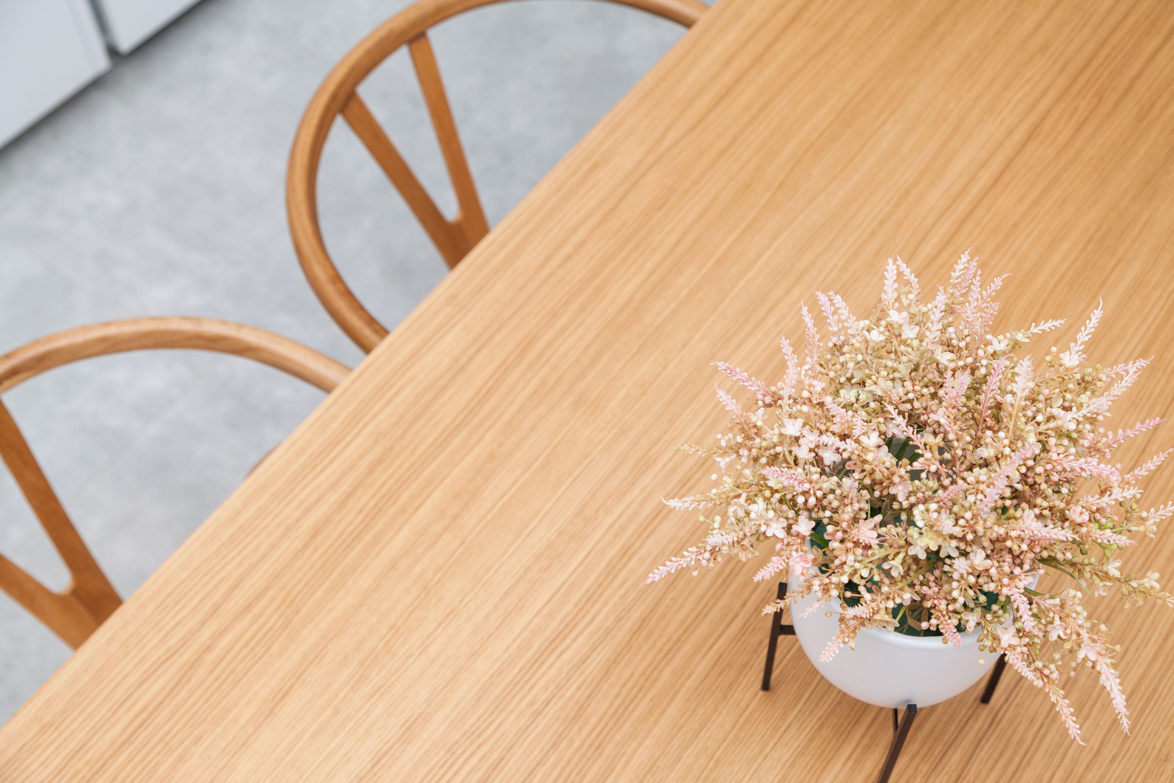 Une table en bois sur laquelle est posé un vase blanc contenant une composition florale.