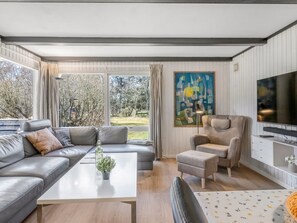 Una sala moderna con sofá, reposapiés, sillón y televisor de pantalla plana.