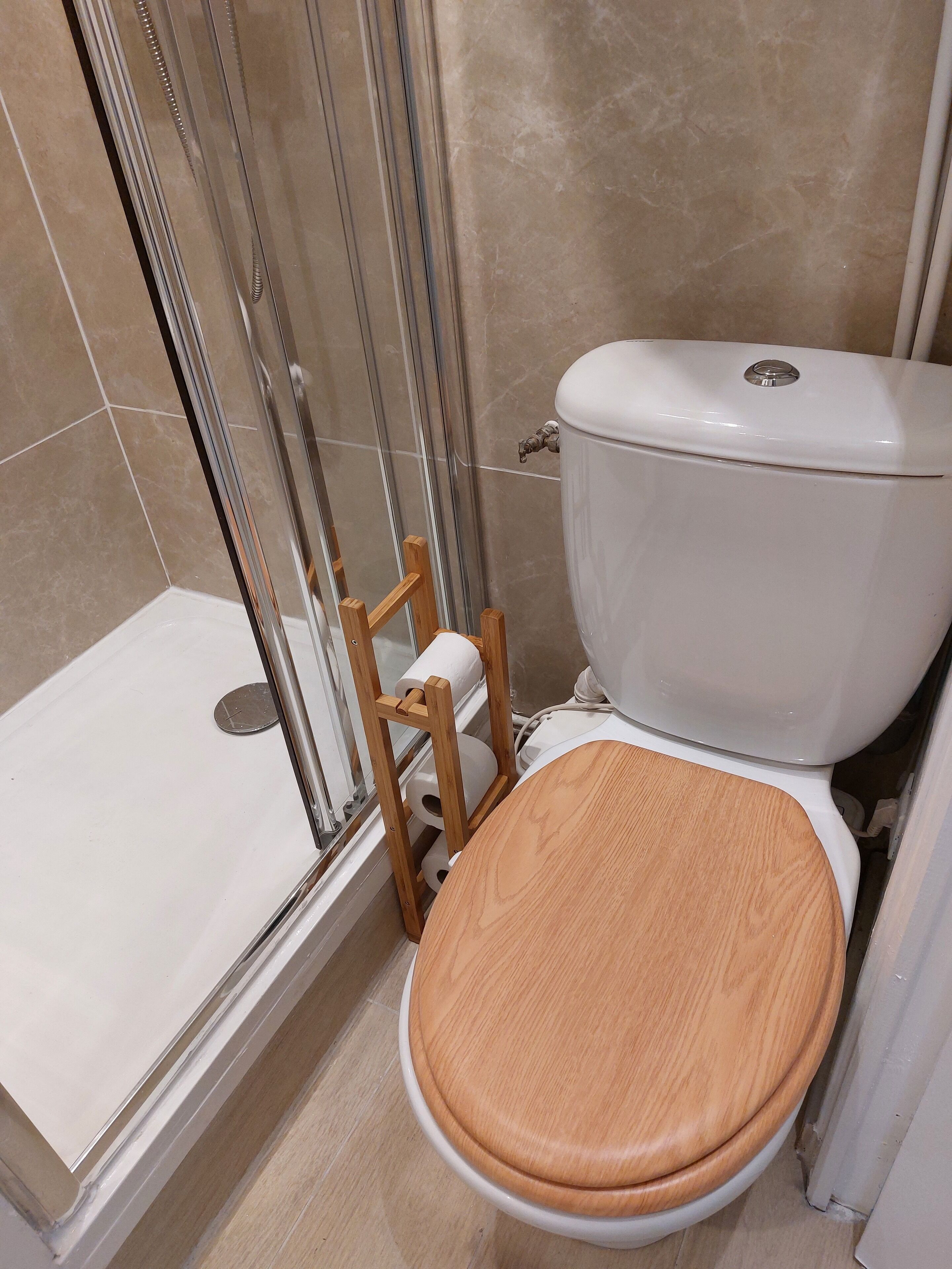 Une salle de bain équipée de toilettes, d’une douche et d’un tabouret en bois.