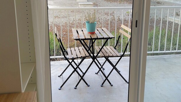 A balcony with a wooden table and chairs, a potted plant, and a view of a building and street. - Studio Notre Dame - Terrace & A/C (Marseille)