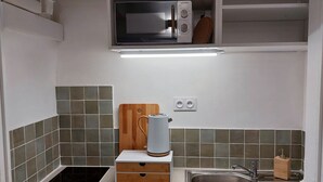 A compact kitchen with a built-in microwave, a kettle, a sink, and a cutting board. - Studio Notre Dame - Terrace & A/C (Marseille)