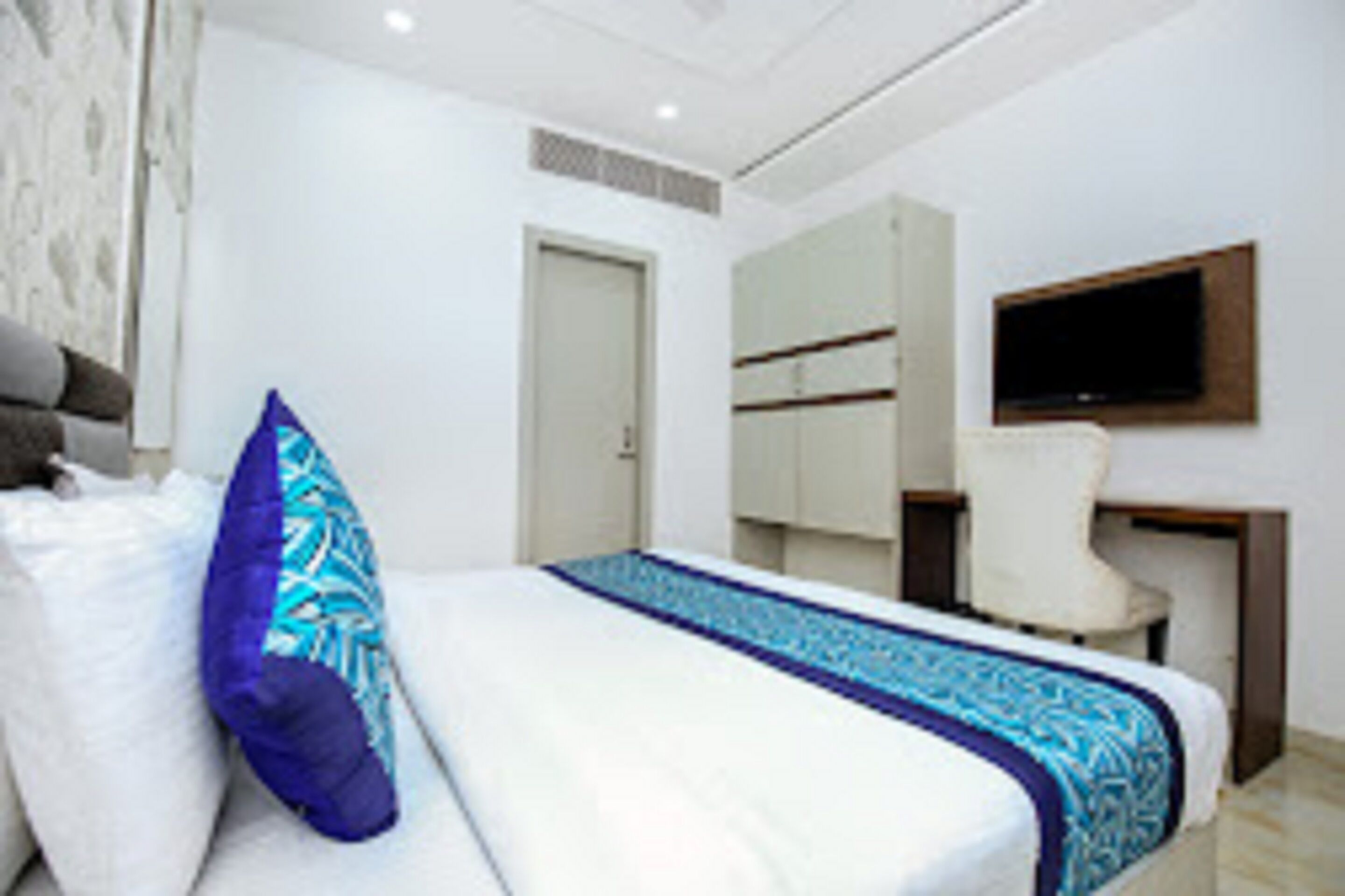 A hotel room with a bed, a chair, a desk, and a television.