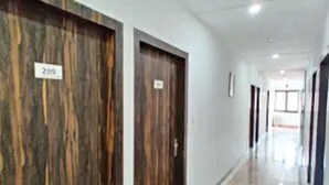 A corridor with wooden doors, each marked with a number. The corridor is well-lit with a shiny floor. - Hotel A Star-50m away from Golden Temple (Amritsar)