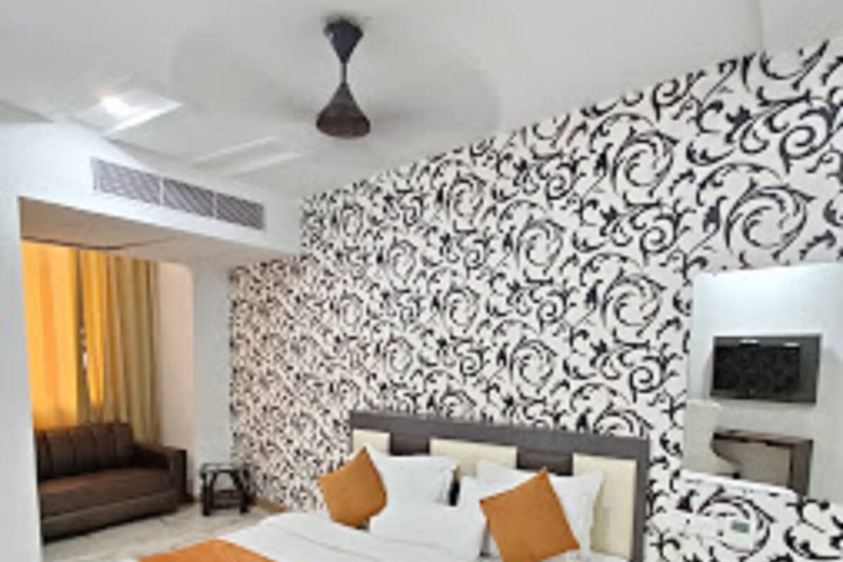 A modern hotel room with a large bed, a bedside table, a wall-mounted TV, and a patterned wallpaper.