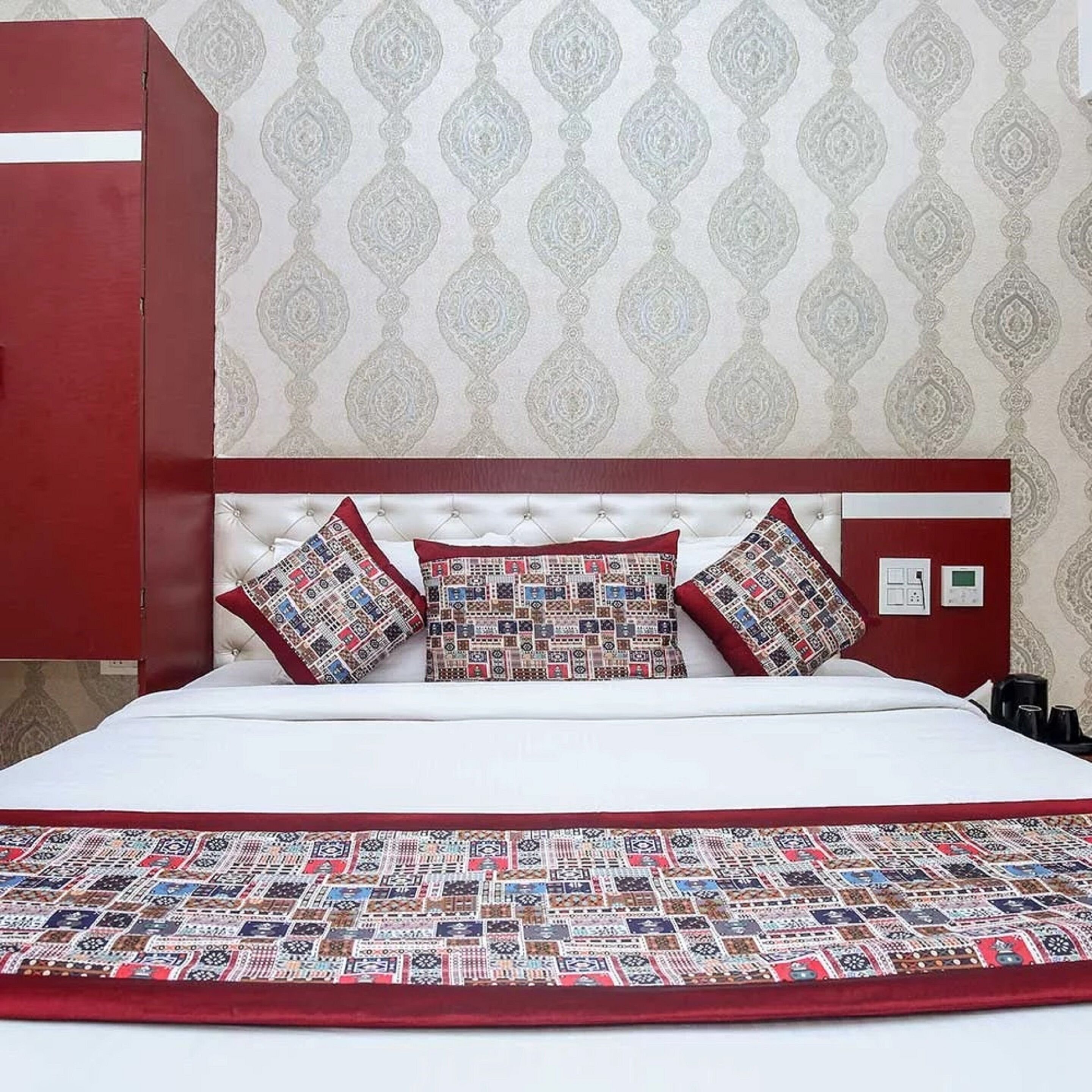A hotel room with a red headboard, patterned pillows, and a red bedspread.