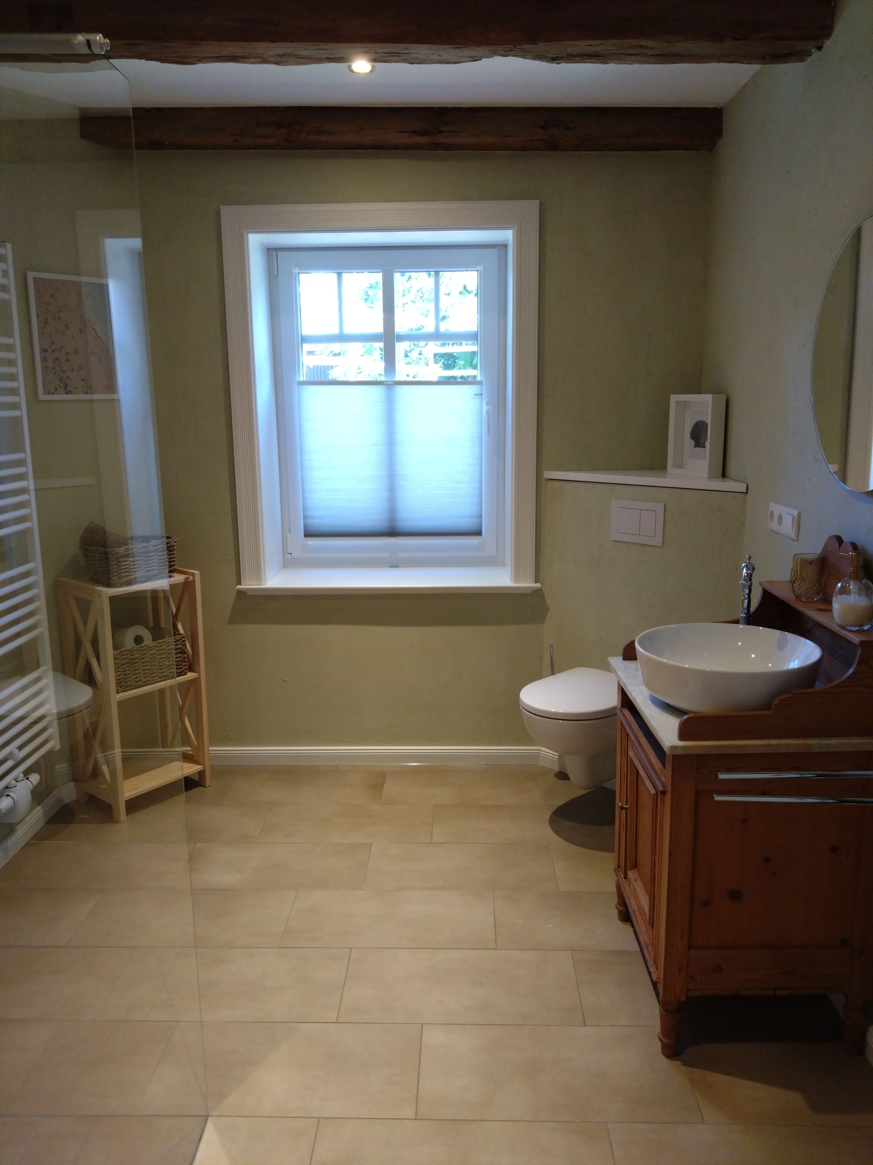 Ein Badezimmer mit Toilette, Waschbecken, Fenster und einem Holzregal.