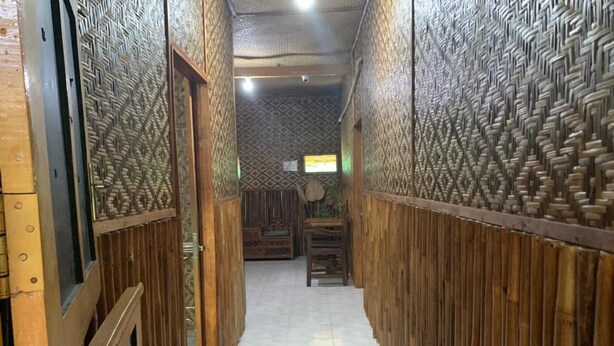 A narrow hallway with wooden paneling and a tiled floor, leading to a room with a patterned wall and a bed. - Bilik Bamboo Homestay (Yogyakarta)