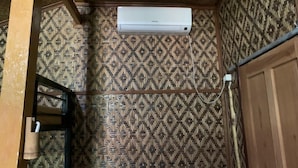 A room with a patterned wall, a wooden door, and an air conditioning unit mounted on the wall. - Bilik Bamboo Homestay (Yogyakarta)