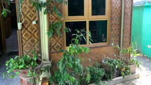 A building with a patterned exterior, a window with a dark frame, and potted plants in front. - Bilik Bamboo Homestay (Yogyakarta)