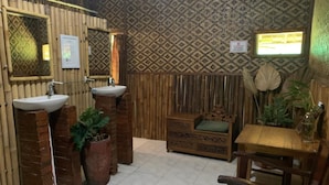 A bathroom with two sinks, a wooden bench, and a patterned wall. - Bilik Bamboo Homestay (Yogyakarta)