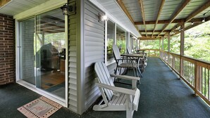 Un porche cubierto con sillas Adirondack, un muro de ladrillo y un puerta corrediza de vidrio que da a un patio.