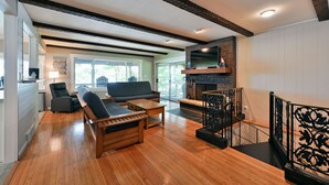 Amplia sala de estar con chimenea, muebles de madera y una escalera con barandillas negras.