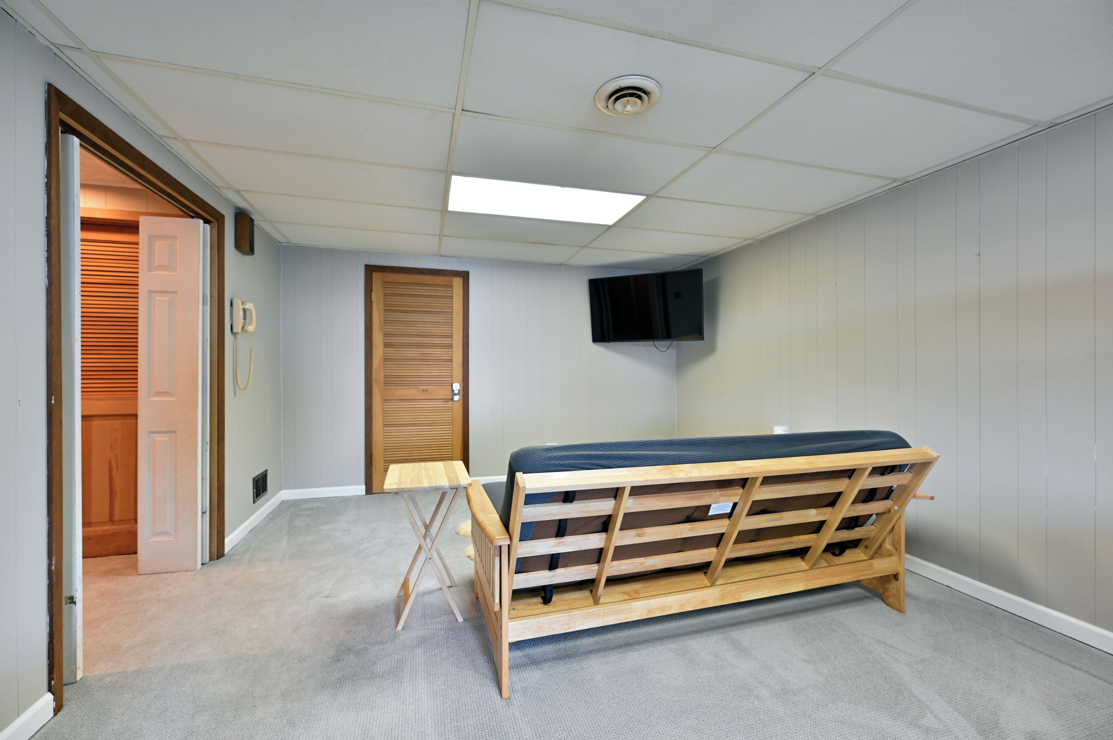 Een kamer met een houten bed, een klein tafeltje, een deur en een wandgemonteerde televisie.