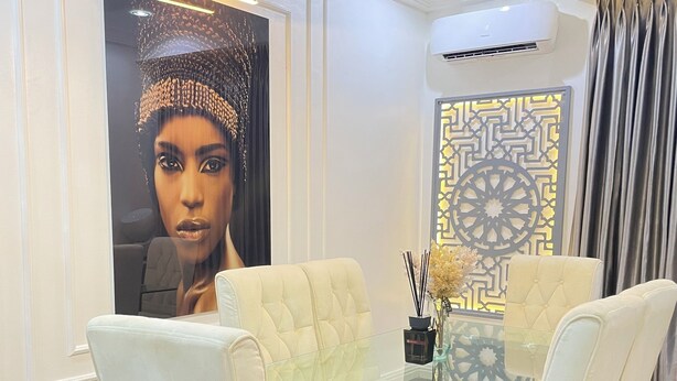 A modern dining room with a glass table, white upholstered chairs, and a decorative wall panel. - Fully fitted 2 bedroom smart luxury apartment. (Abuja)