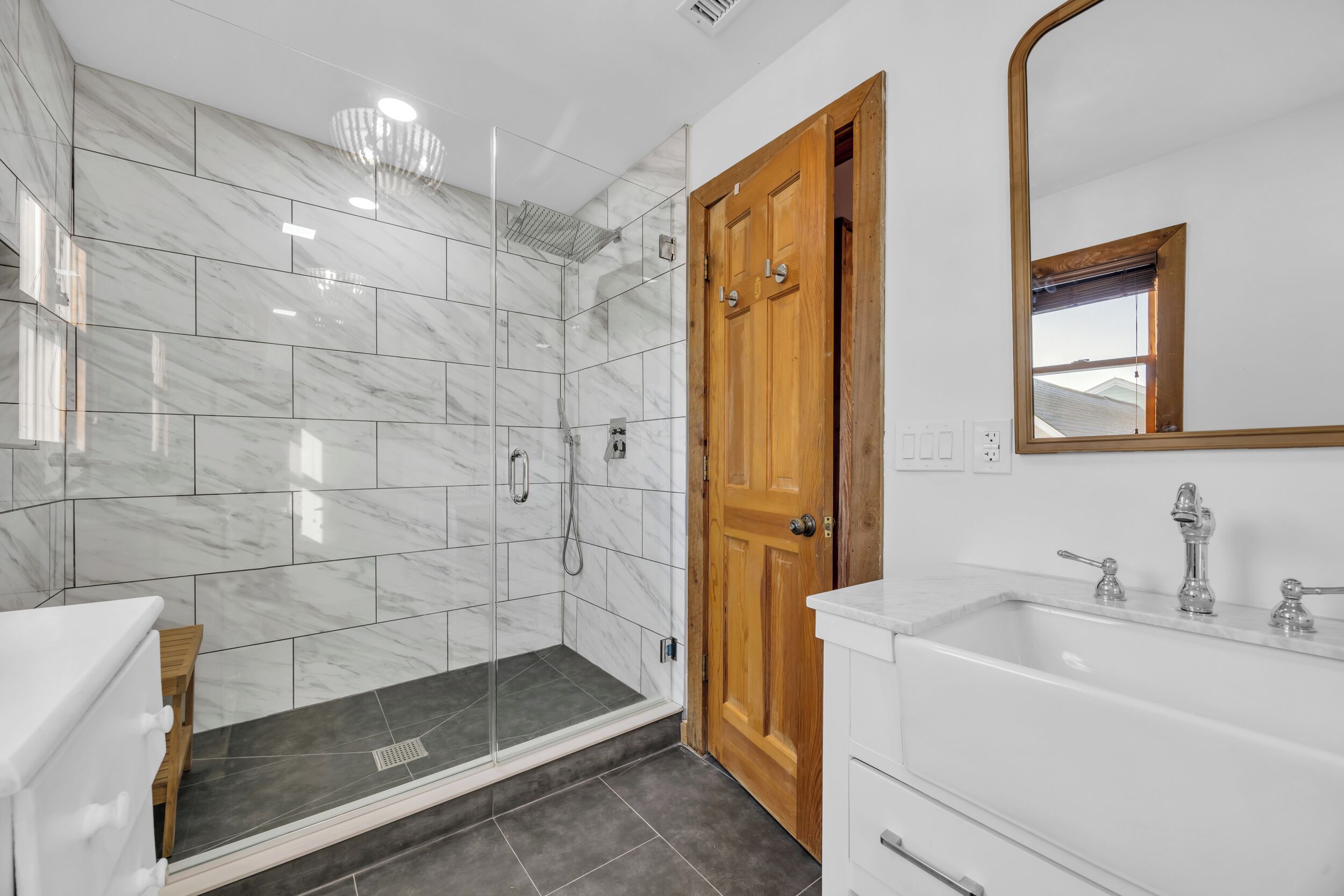 A bathroom with a glass-enclosed shower, a wooden door, and a white sink with a mirror.