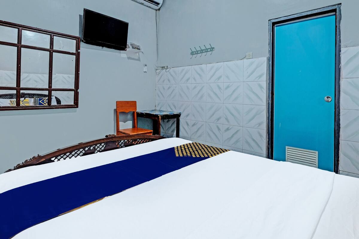 Una habitación de hotel con una cama, televisión montada en la pared, una ventana y una puerta.