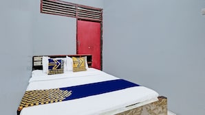Een bed met een witte matras, een deken met blauw en geel dessin en twee kussens met geometrische patronen.