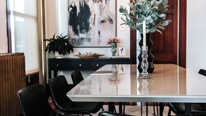 A dining area with a long table, black chairs, a vase with greenery, and a large abstract painting on the wall. - LUX Uptown Escape - The Trester
 (Sheboygan)