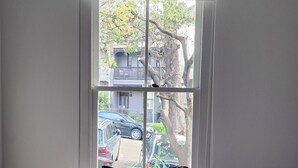 A bedroom with a large bed, a window with a view of the street, and a hanging light fixture.