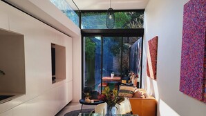 A modern interior with a glass dining table, white sofas, and a large window offering a view of the outdoors.