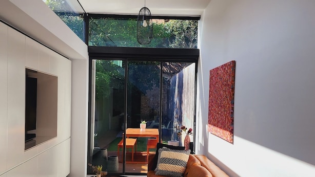 A modern living room with a glass table, a sofa, and a TV mounted on the wall.