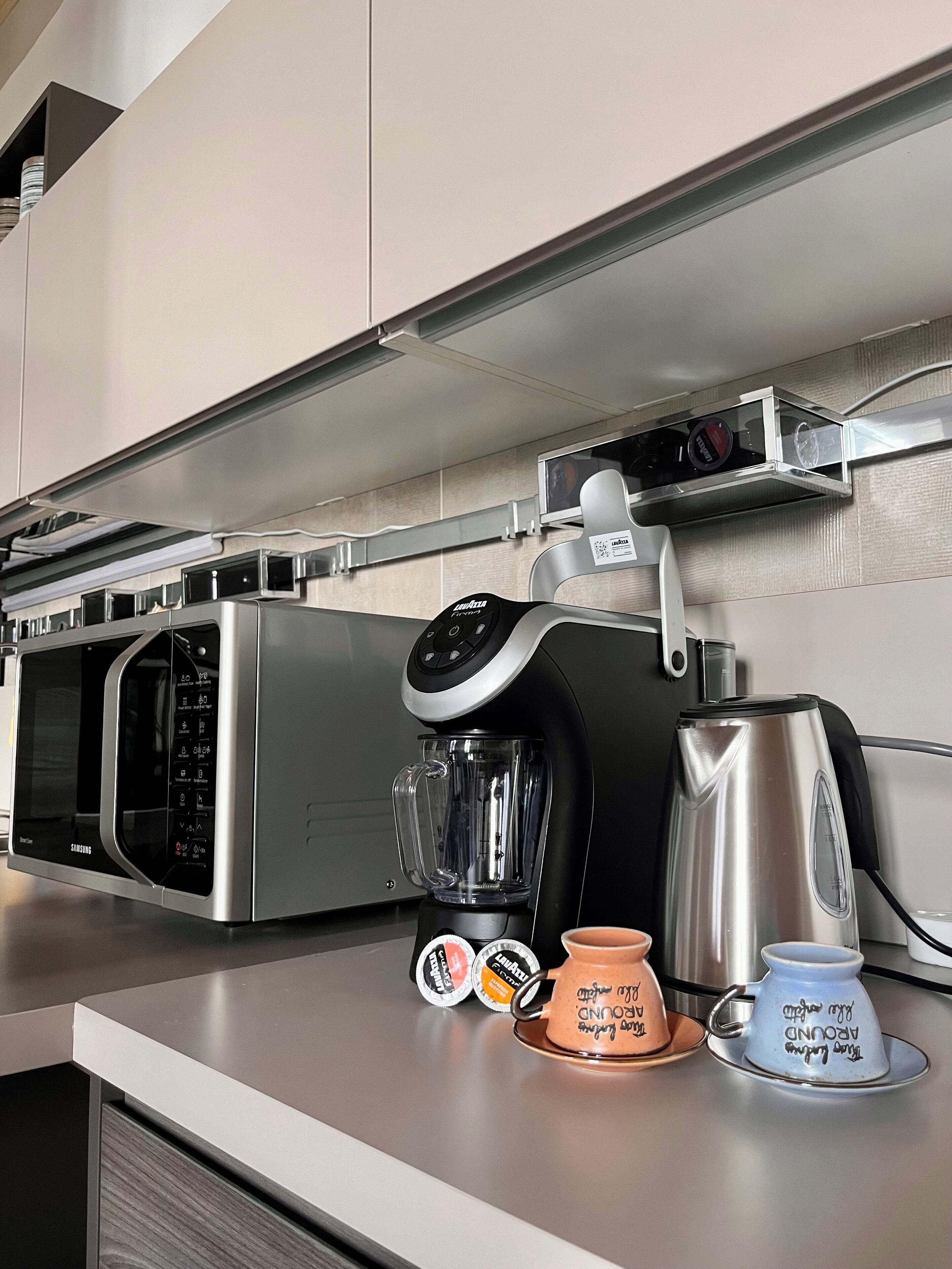 A kitchen with a microwave, coffee maker, and two cups on the counter.
