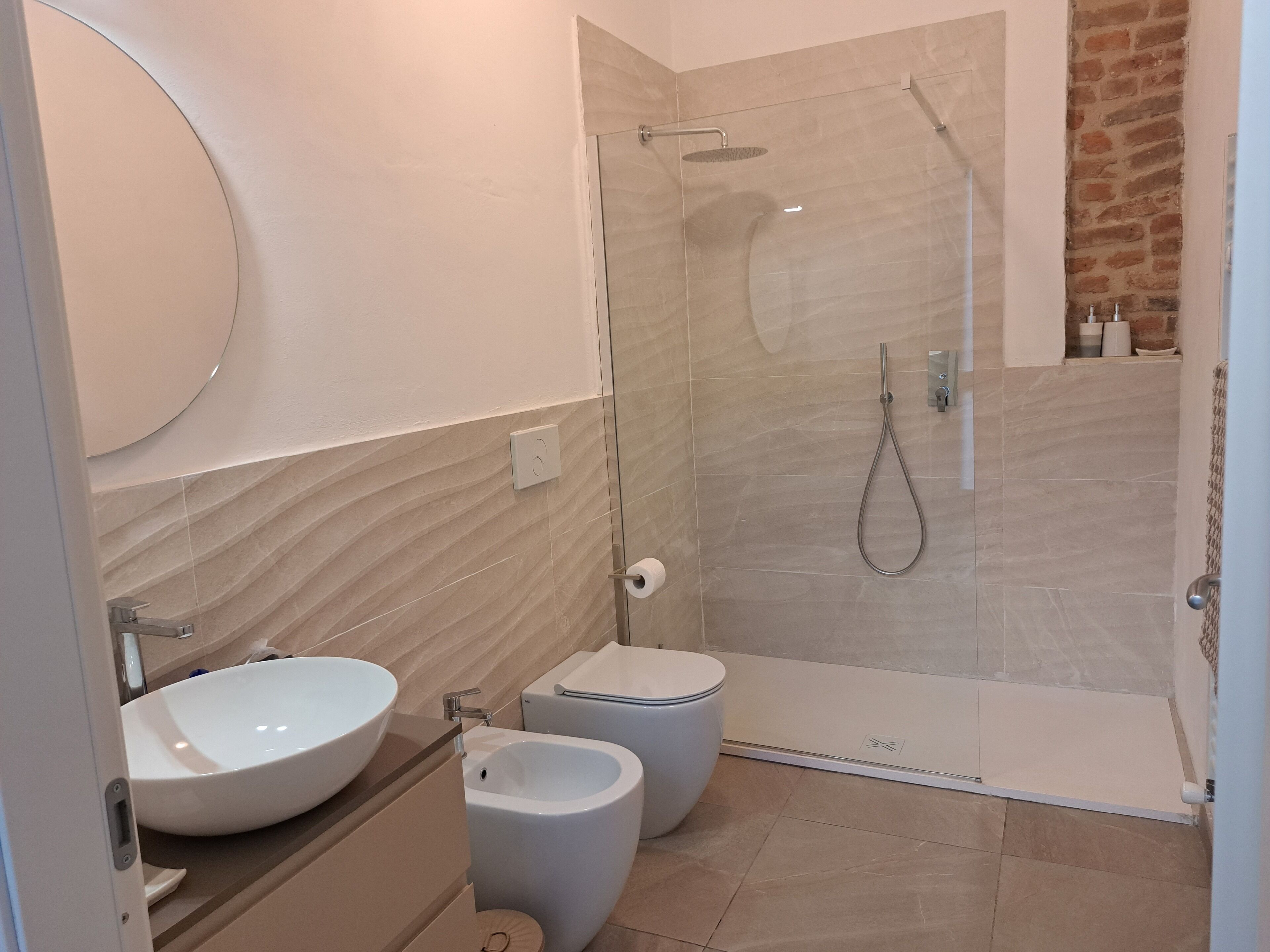 A modern bathroom with a large round sink, a bidet, a glass-enclosed shower, and a toilet.