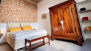Une chambre avec un mur en briques, une armoire en bois, un lit avec une banquette et un plafond orné de motifs floraux.