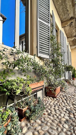 A cobblestone street with potted plants and shutters on a building. - Dimora Boezio7, elegant apartment in the center (Pavia)