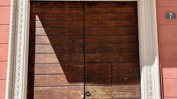 Una puerta doble de madera con un picaporte de latón, enmarcada por un elaborado moldura blanca, sobre un pared rosa con un letrero con el número '7'.